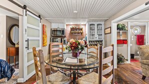 A dining area with a glass table, wicker chairs, a vase of flowers, and a brick wall with shelves.
