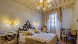 A classic bedroom with a large bed, ornate wall sconces, a chandelier, and a window with curtains. - Appartamento Zefferini (Cortona)