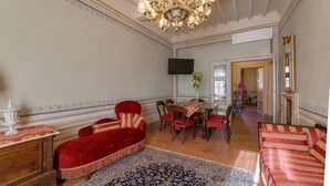A spacious room with a large chandelier, a dining table with chairs, a red sofa, and a patterned rug. - Appartamento Zefferini (Cortona)