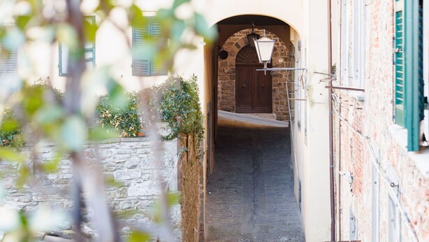 A narrow alleyway with a stone wall on one side and a building with green shutters on the other. - Appartamento Zefferini (Cortona)