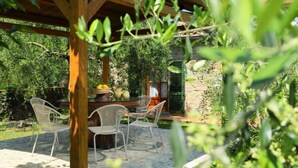 Eine Terrassengestaltung im Freien mit einer Holz-Pergola, Steinboden und weißen Metallstühlen.