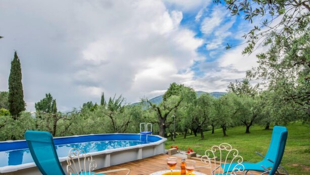 An outdoor pool area with blue chairs and a table, surrounded by trees and a mountainous backdrop. - Il Fienile del Colle by Interhome (Pescia)