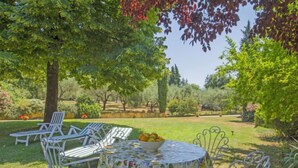 An outdoor seating area with a round table and chairs, surrounded by lush greenery and trees. - Il Fienile del Colle by Interhome (Pescia)