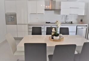 Une cuisine moderne avec des armoires blanches, un four en acier inoxydable, une cuisinière à gaz et un lave-vaisselle. On y trouve une table à manger avec quatre chaises et un vase rempli de fleurs posé sur la table.