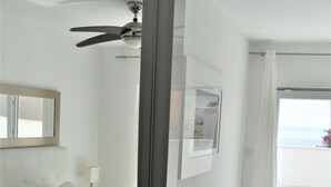 A modern hotel room with a bed, a ceiling fan, a balcony with a white chair, and a view of the ocean.