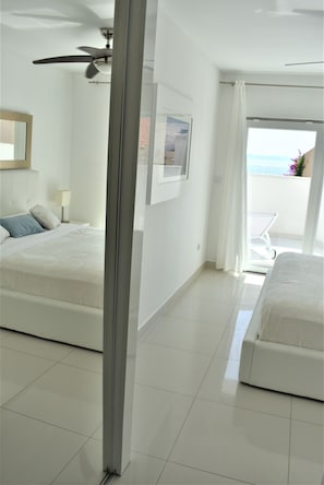 Une chambre d’hôtel avec deux lits, un ventilateur de plafond, un balcon avec une chaise et une vue sur la mer.