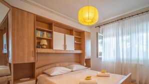 Un dormitorio con cama, armario de madera, estanterías y lámpara de noche.
