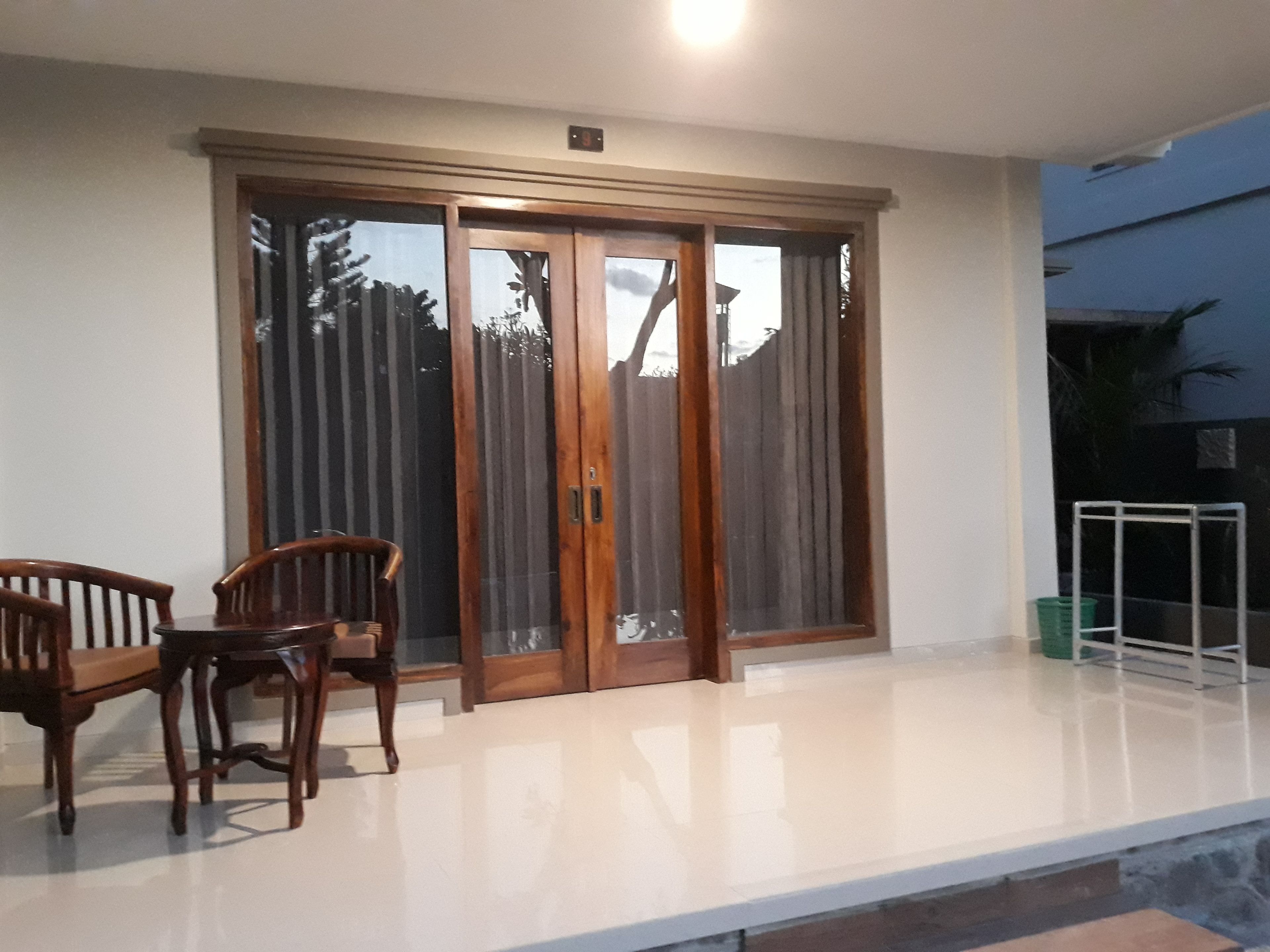 Un patio con puerta corredera de vidrio, una mesa de madera con sillas y un pequeño jardín delimitado por una valla metálica.