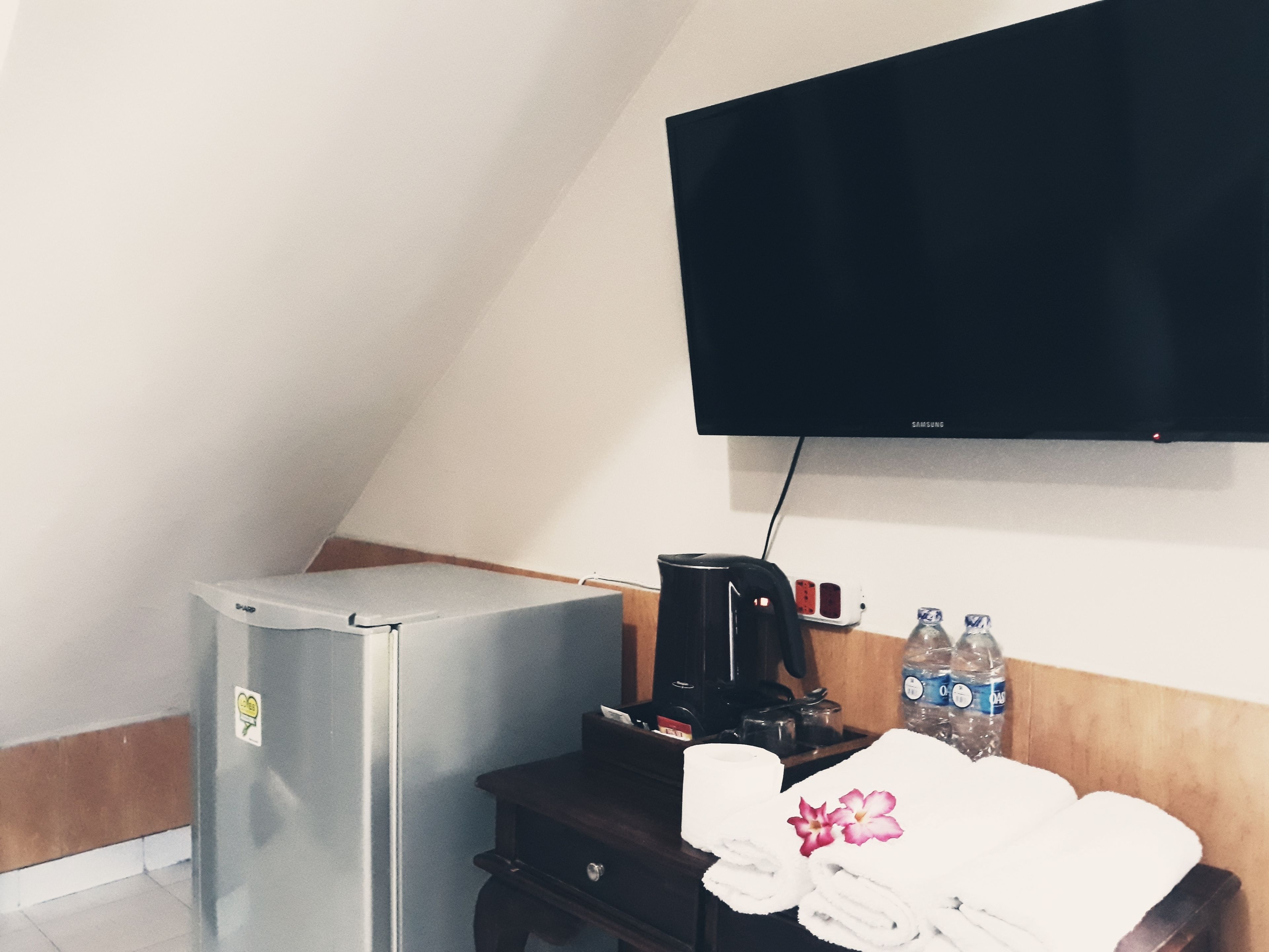 Una pequeña kitchenette con refrigerador, cafetera y una botella de agua sobre una mesa de madera.