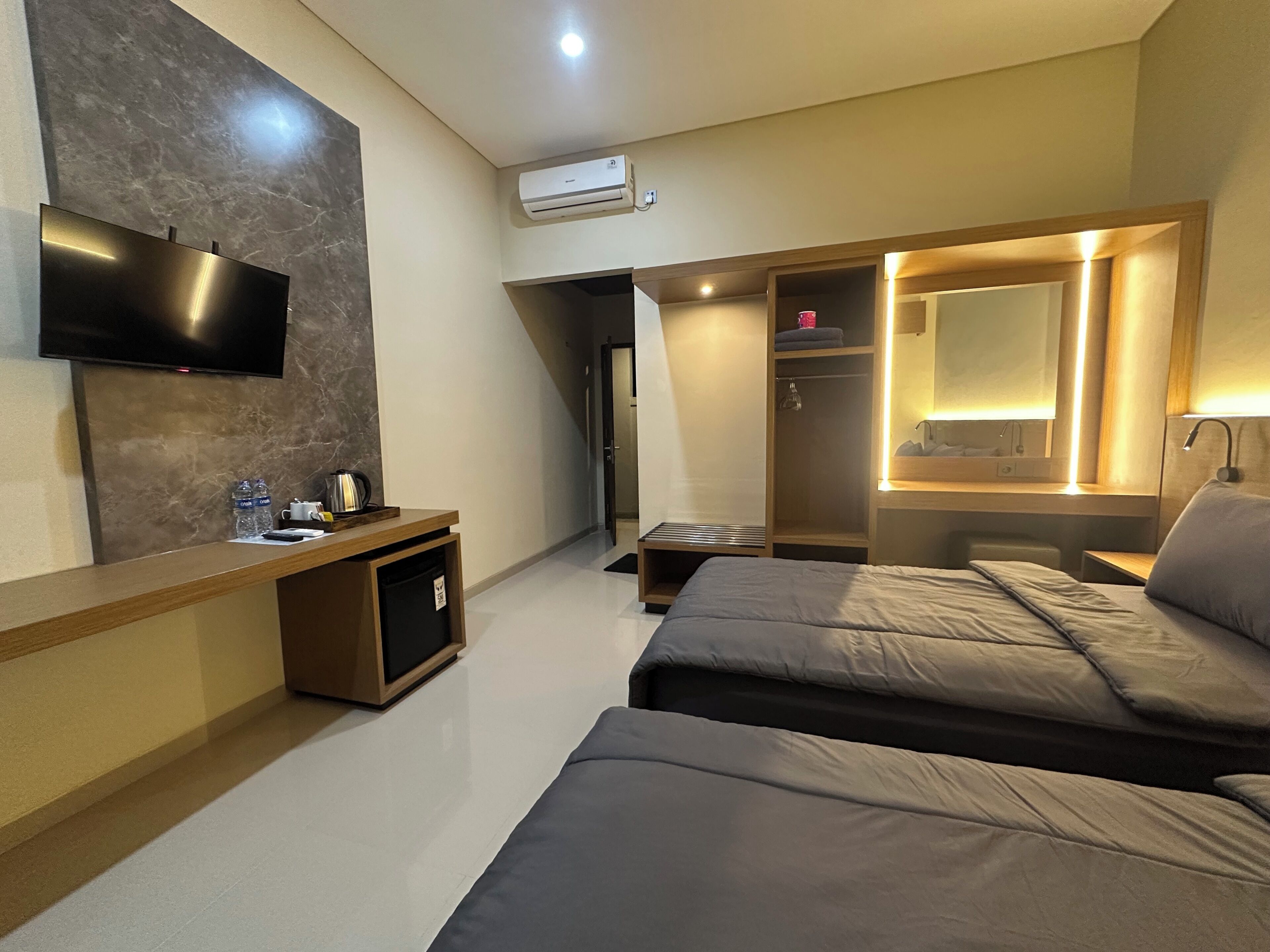 A modern hotel room with a flat-screen TV, a desk with a coffee maker, a wardrobe, and a bed.