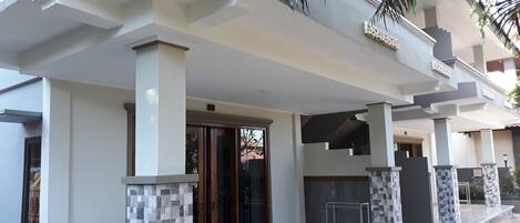 A modern house with a covered porch, tiled columns, and a staircase leading to a balcony.