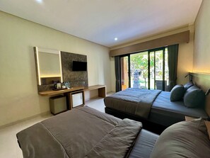Una habitació d'hotel amb un llit, escriptori, televisió de pantalla plana, mini-nevera i finestra amb vista a vegetació.