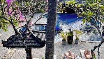 A pool area with lounge chairs, a palm tree, and a traditional tiled roof structure.