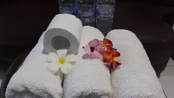 Una bandeja con tres toallas blancas enrolladas, una flor blanca y una flor rosa y amarilla. En el fondo, tres botellas de agua con tapones azules.