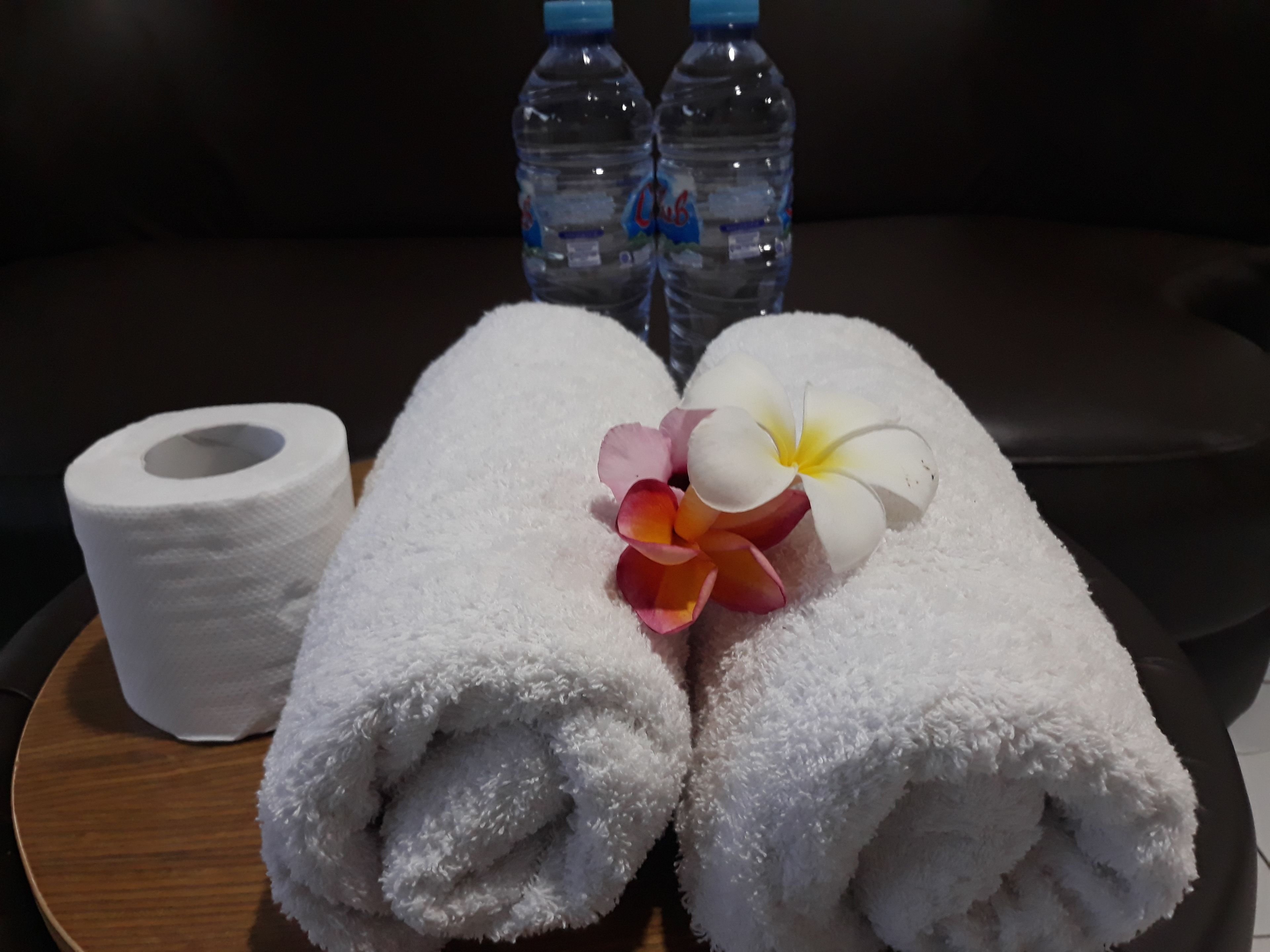 Two rolled white towels and a roll of toilet paper on a wooden tray.