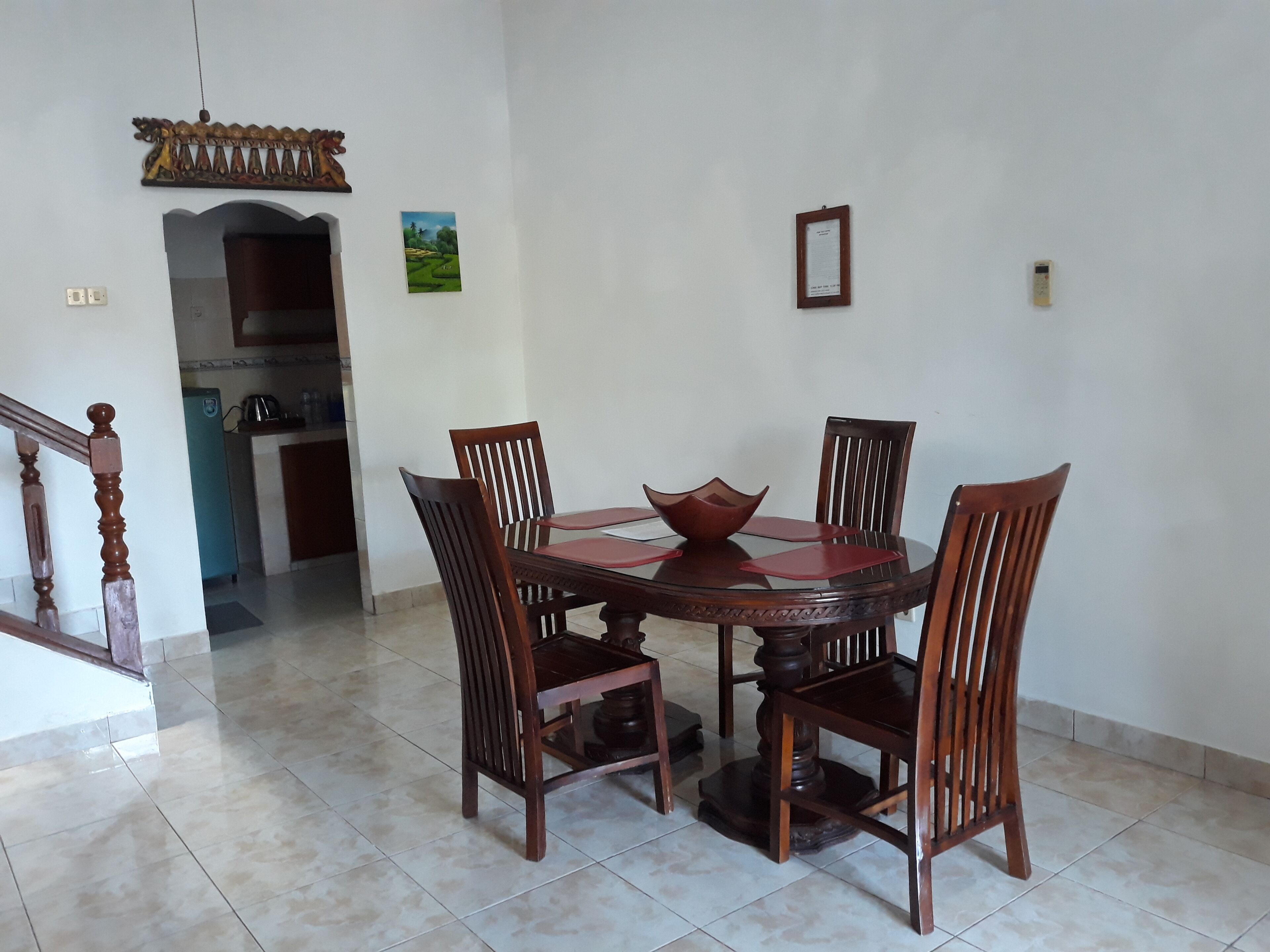 A dining area with a round wooden table and six chairs, a decorative bowl on the table, and a small painting on the wall.