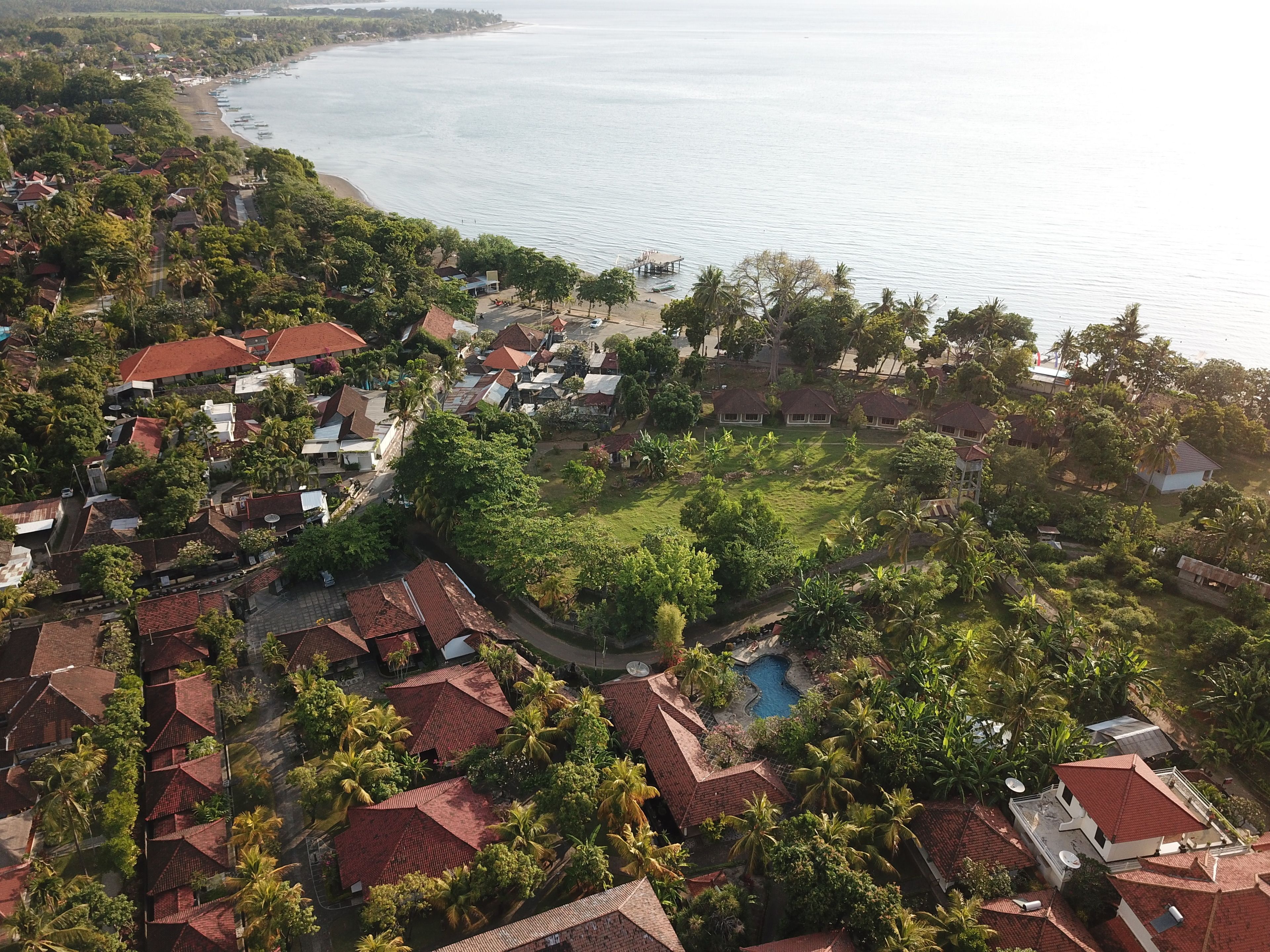An aerial view of a coastal residential area with houses, a beach, and a swimming pool.