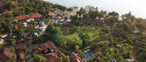 Ovenfra ses et kystnære boligområde med huse, strand og swimmingpool.