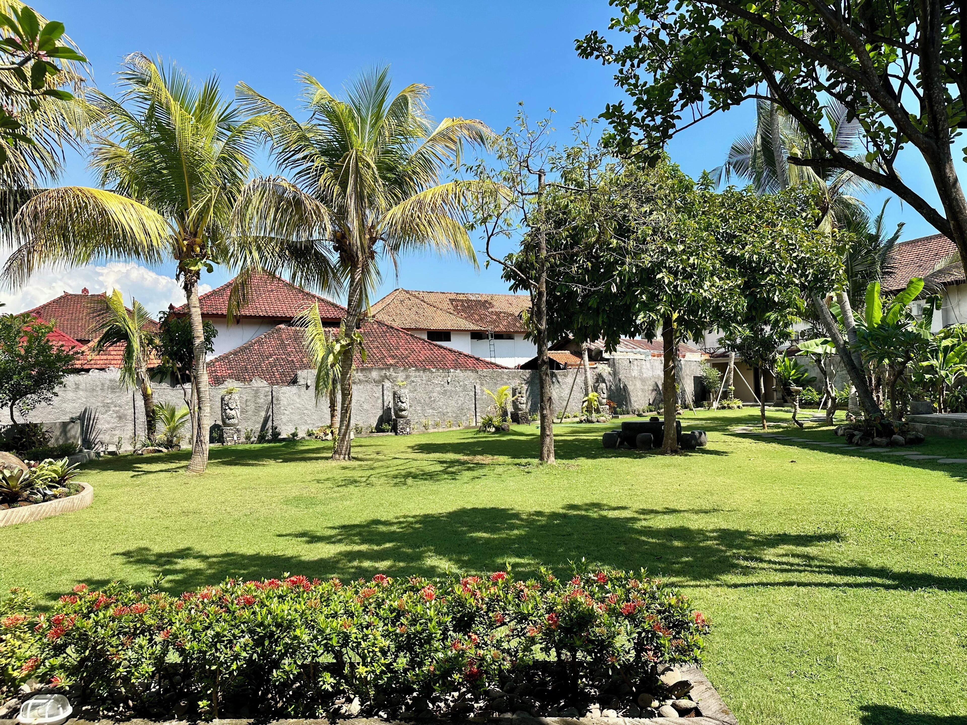 A courtyard with palm trees, a stone wall, and a building with red-tiled roofs.