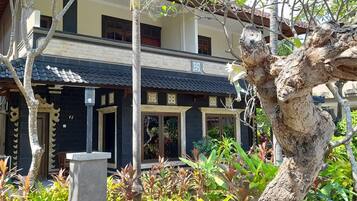 Un edificio tradicional con tejado de baldosas, balcón y jardín con diversas plantas.