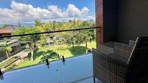 Un balcón con una silla de mimbre, vista a un jardín con palmeras y cielo despejado.