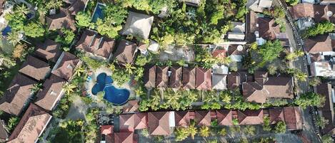 An aerial view of a residential area with houses, a swimming pool, and surrounding greenery.
