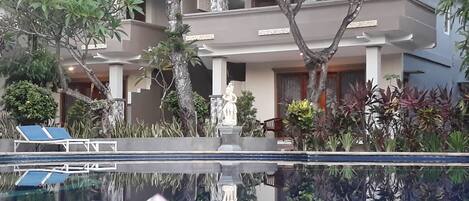 A modern building with a swimming pool, surrounded by various plants and a statue.