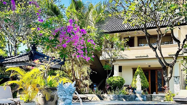 Una piscina con fuentes, rodeada de exuberante vegetación y un edificio tradicional.