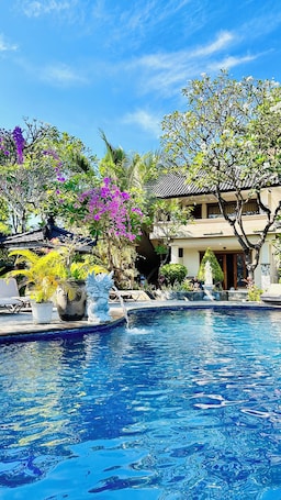 A swimming pool with water features, surrounded by lush greenery and a traditional building.