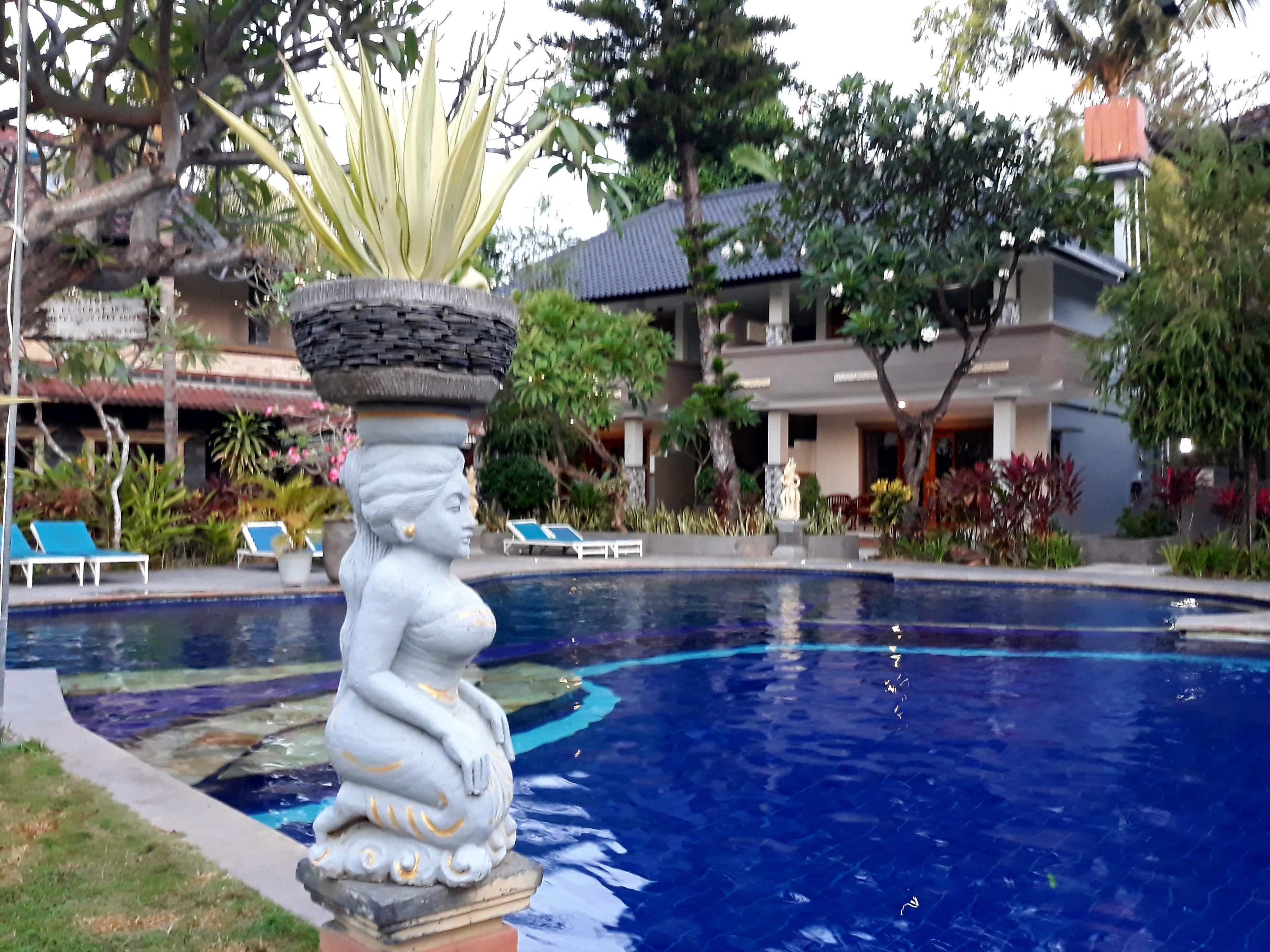 A statue of a seated figure with a pedestal, a pool, and a building with a tiled roof in the background.
