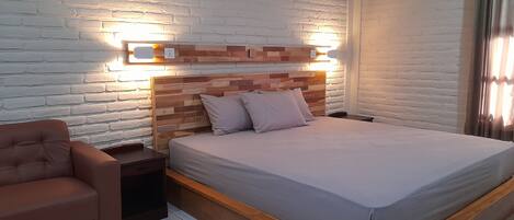 A bedroom with a wooden headboard, a bed with a grey mattress, a brown armchair, and a nightstand.