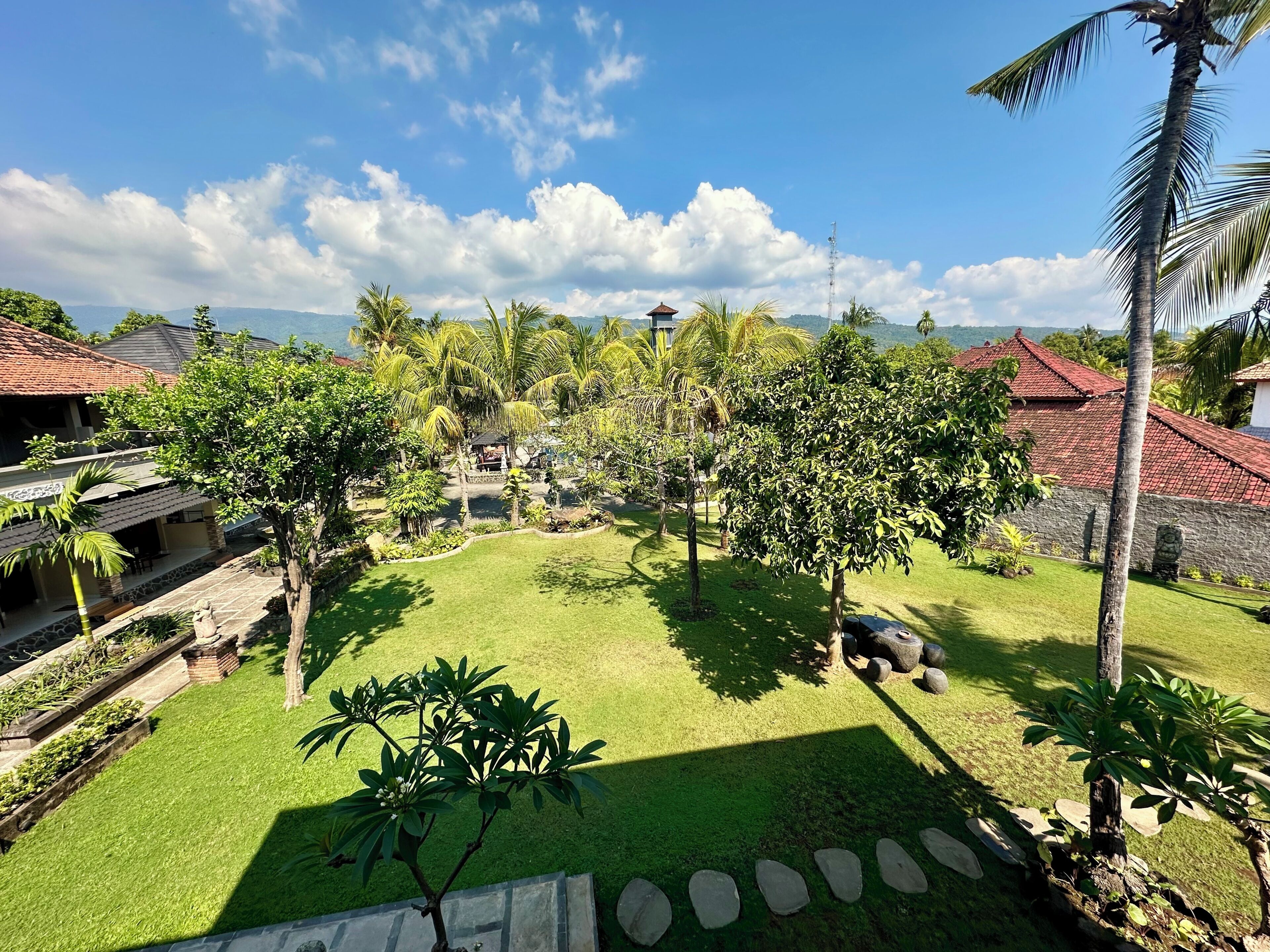 Un jardín tropical con palmeras, un sendero de piedra y vista al mar.