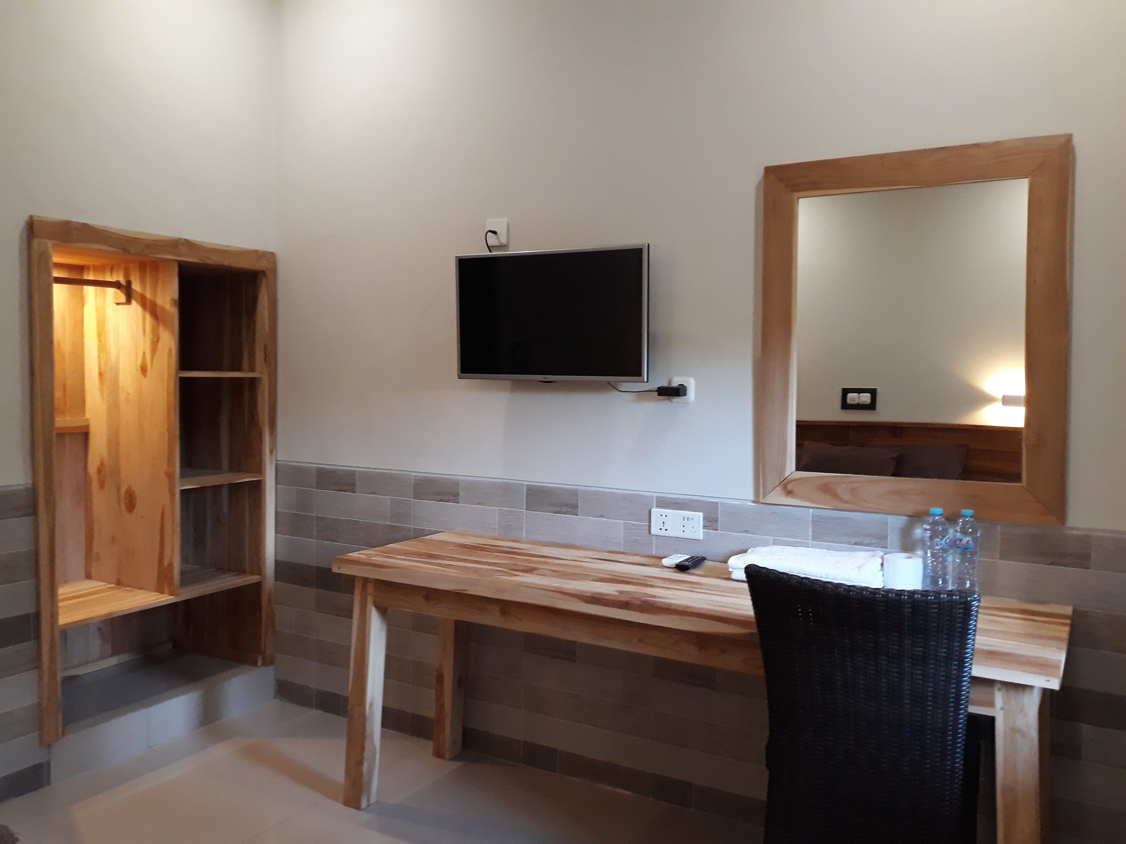 A bathroom with a wooden vanity, a mirror, a television mounted on the wall, and a tiled backsplash.
