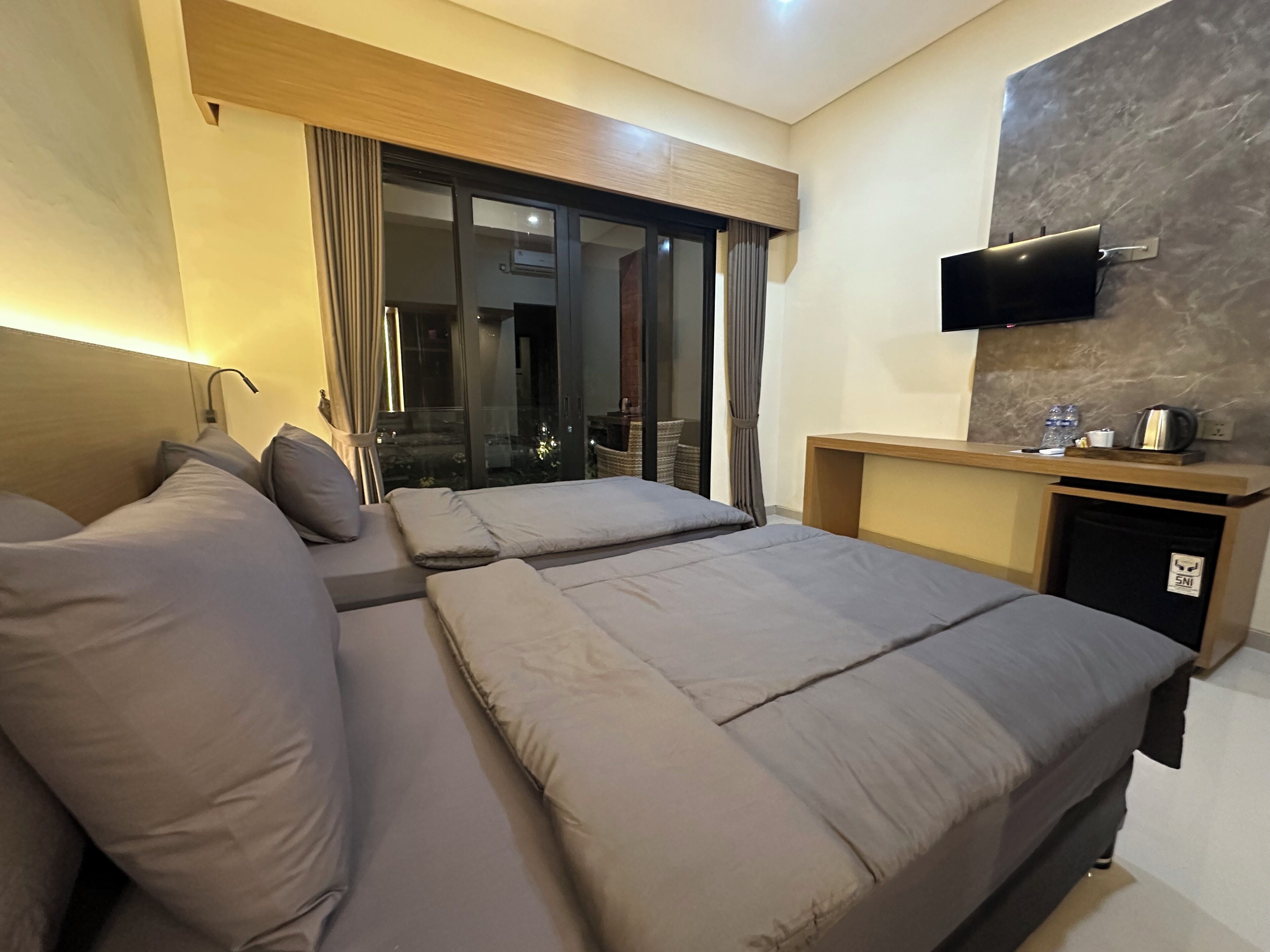 A modern hotel room with a large bed, a TV mounted on the wall, and a small desk with a kettle.