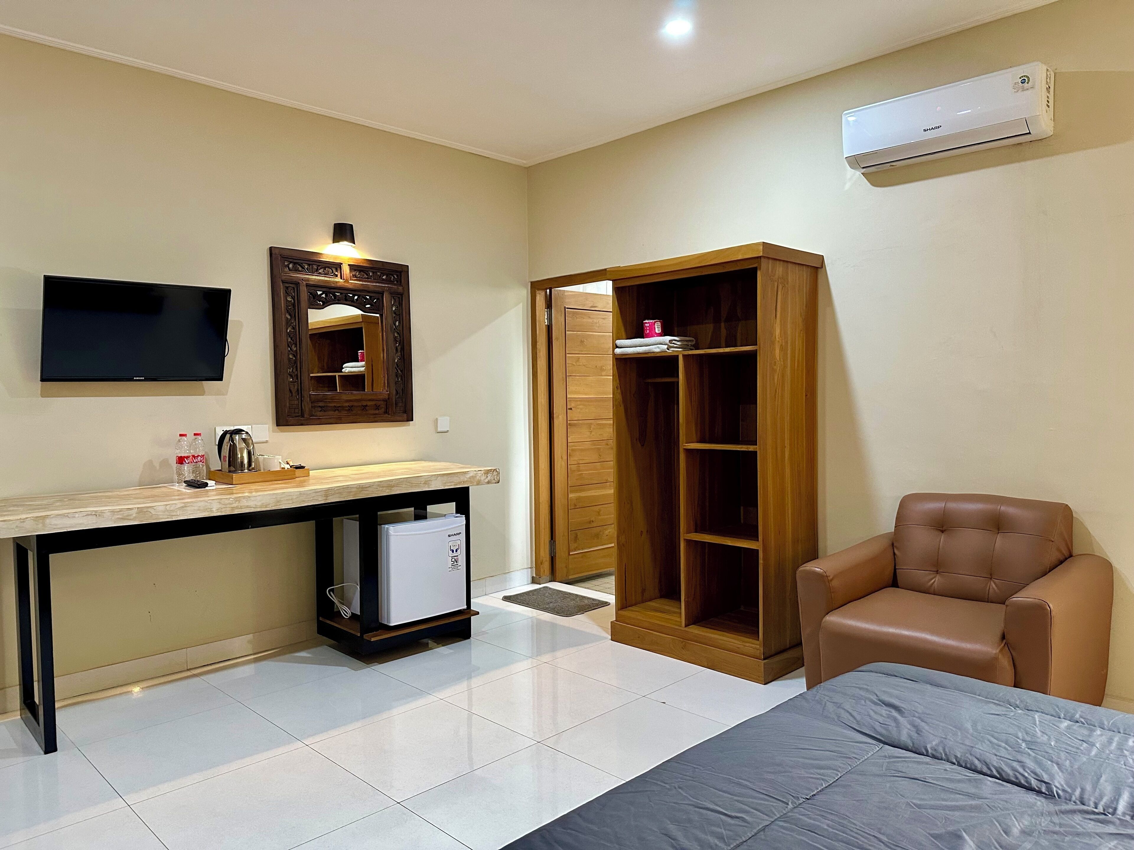 Habitación de hotel con televisión de pantalla plana, armario de madera, sillón de cuero y minibar.