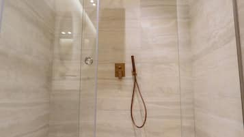 Una ducha moderna con puerta de cristal, paredes de mármol y cabezal de madera.