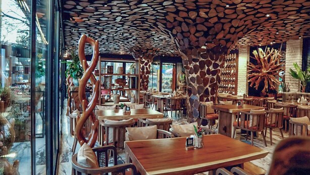 Interior de un restaurante con un diseño de techo singular, mesas y sillas de madera, y vistas al exterior.