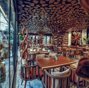 Interior de un restaurante con un diseño de techo singular, mesas y sillas de madera, y vistas al exterior.