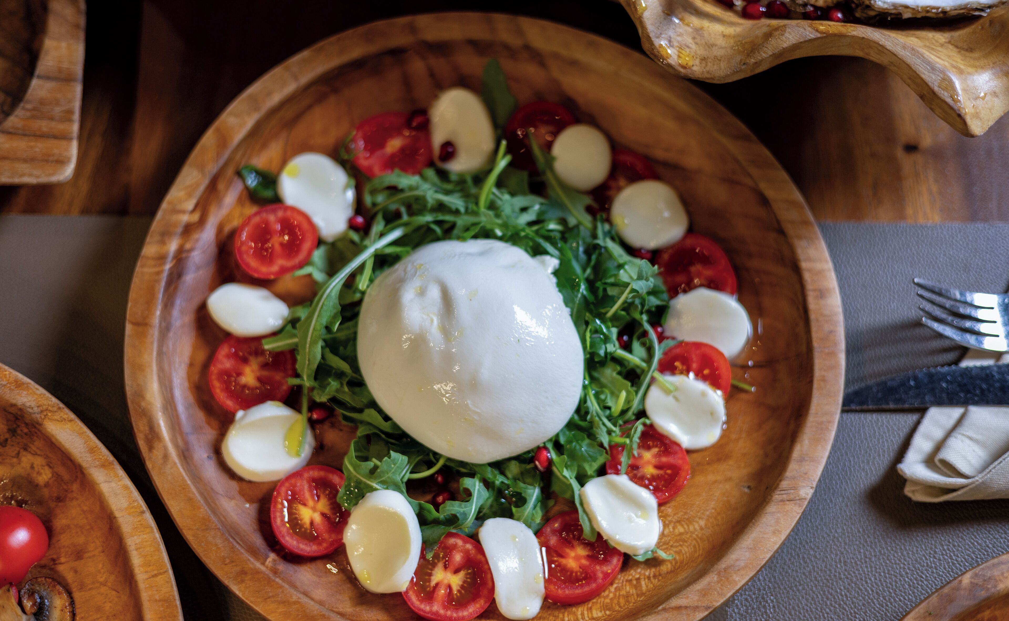 A wooden bowl with a salad of arugula, cherry tomatoes, and mozzarella balls.
