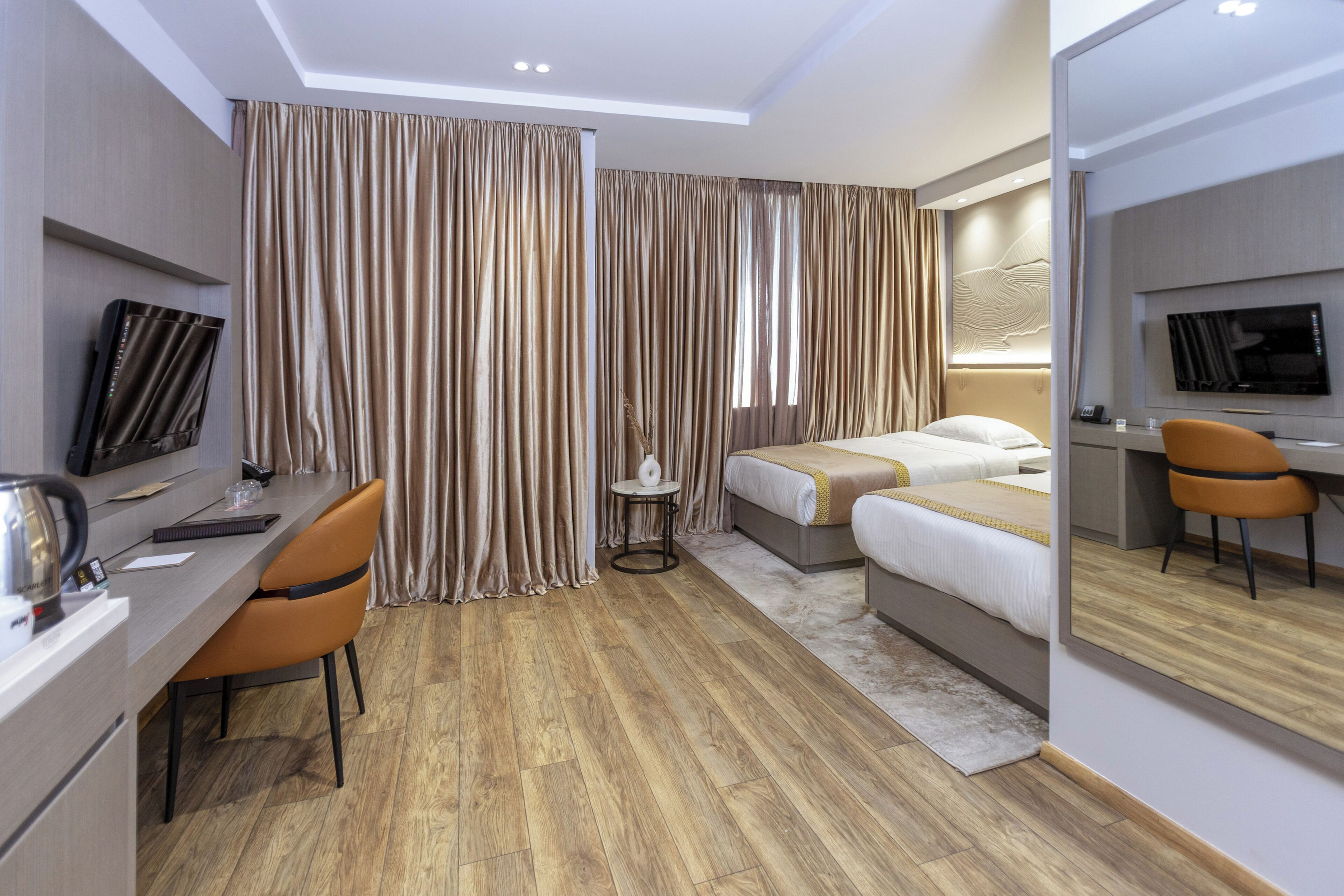 A hotel room with a desk, two beds, a TV, and a mirror.