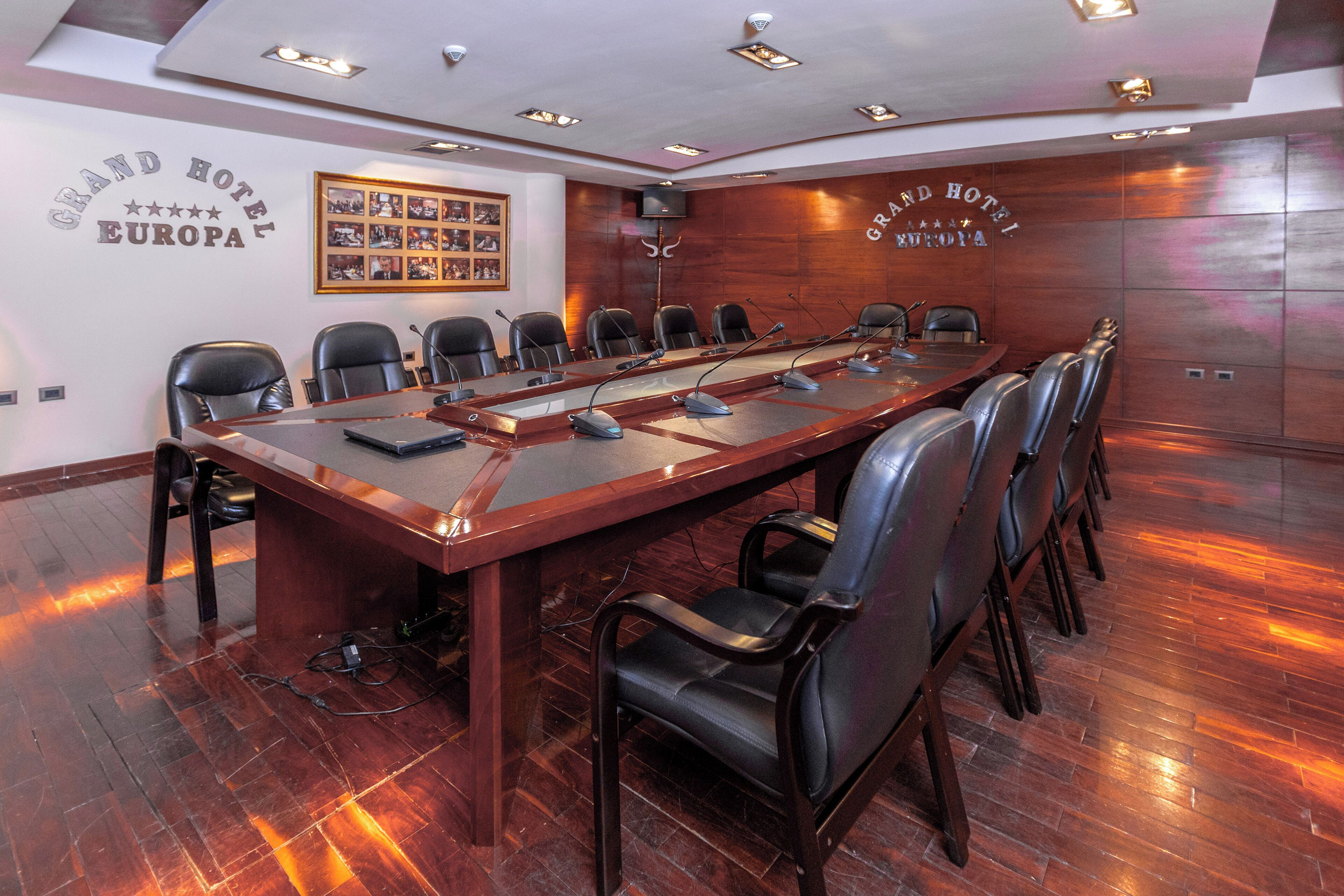 A conference room with a long table, black leather chairs, and a wooden panel wall with the hotel name.