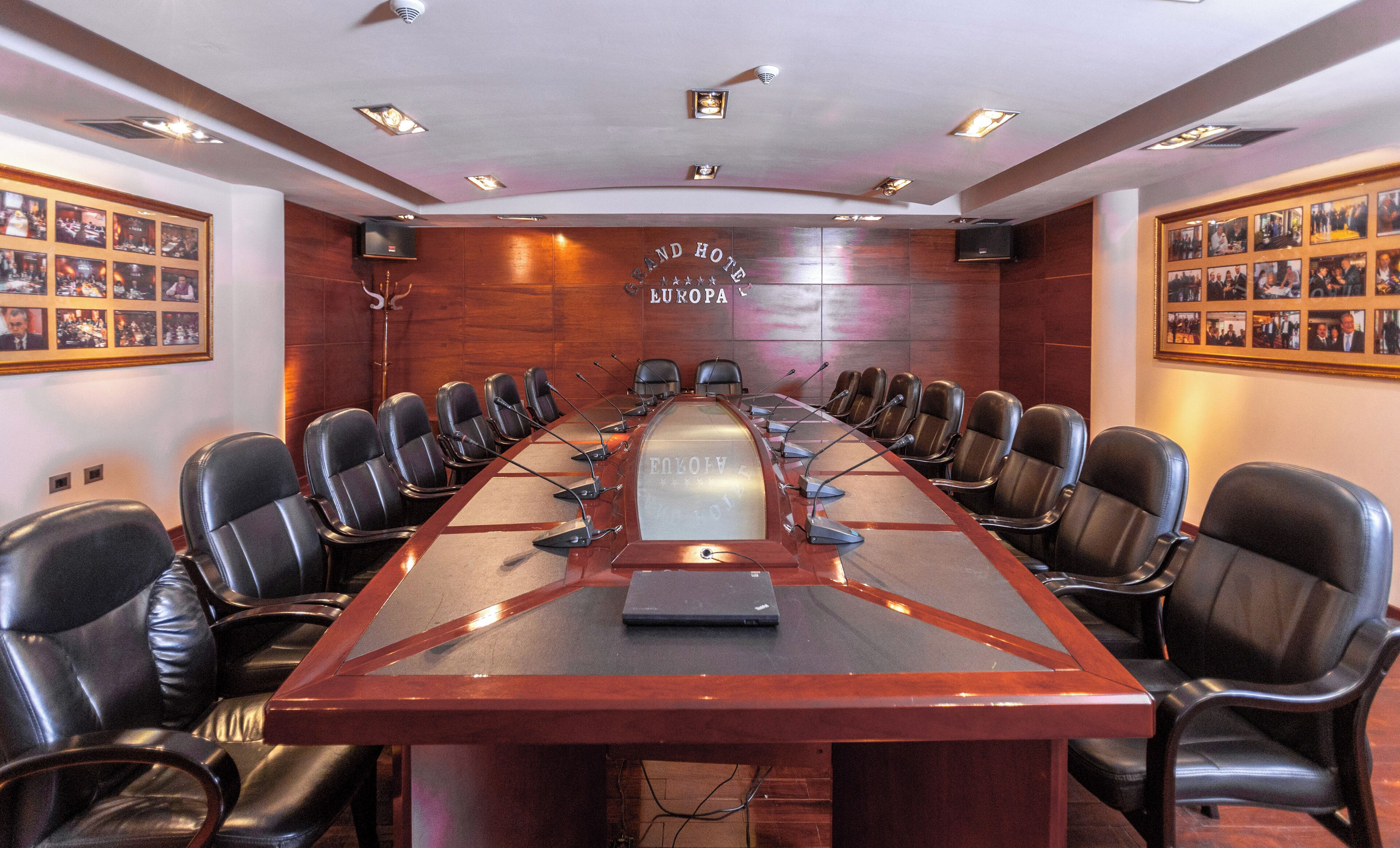 Una sala de conferencias con una larga mesa, sillas de cuero y un ordenador portátil sobre la mesa.