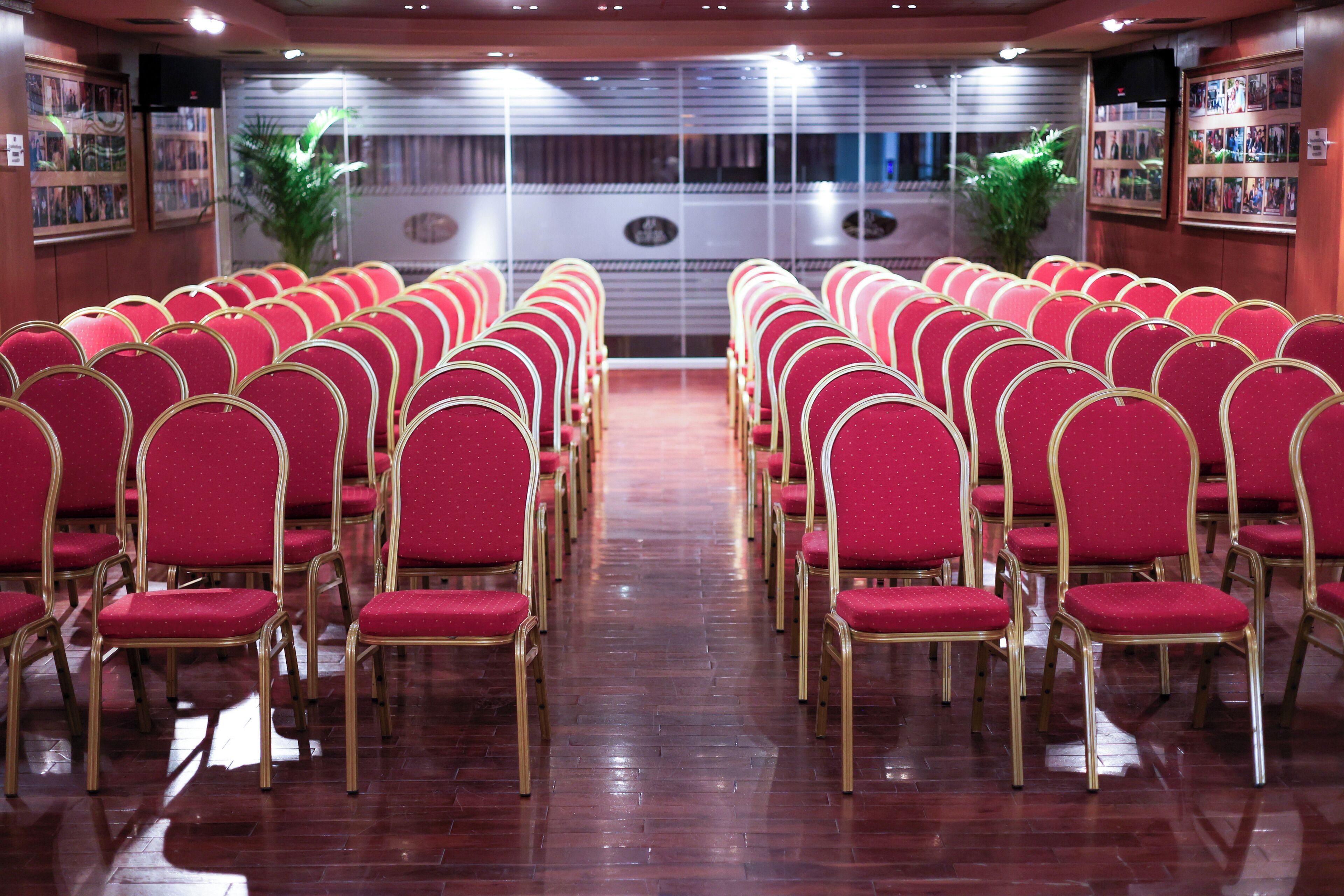 Rows of red chairs with gold frames arranged in a hall with a polished wooden floor.