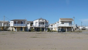 Un conjunto de casas de playa con balcones, un primer plano de arena y un cielo azul despejado.