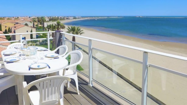 Un balcón con una mesa lista para comer, con vista a una playa y el océano.