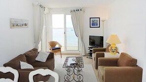 Una sala de estar con un sofá, un sillón y una mesa de centro. Hay un televisor y una lámpara.