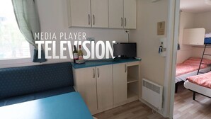 Une pièce compacte comprenant un coin cuisine, un petit espace salon, un téléviseur et un lit superposé.