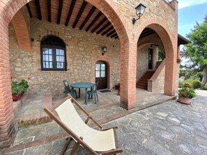 A stone building with a covered patio, a table with chairs, and a lounge chair. - Olenadro by Interhome (Volterra)