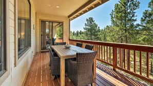 Terraza de madera con mesa y sillas, con vista a un área boscosa.