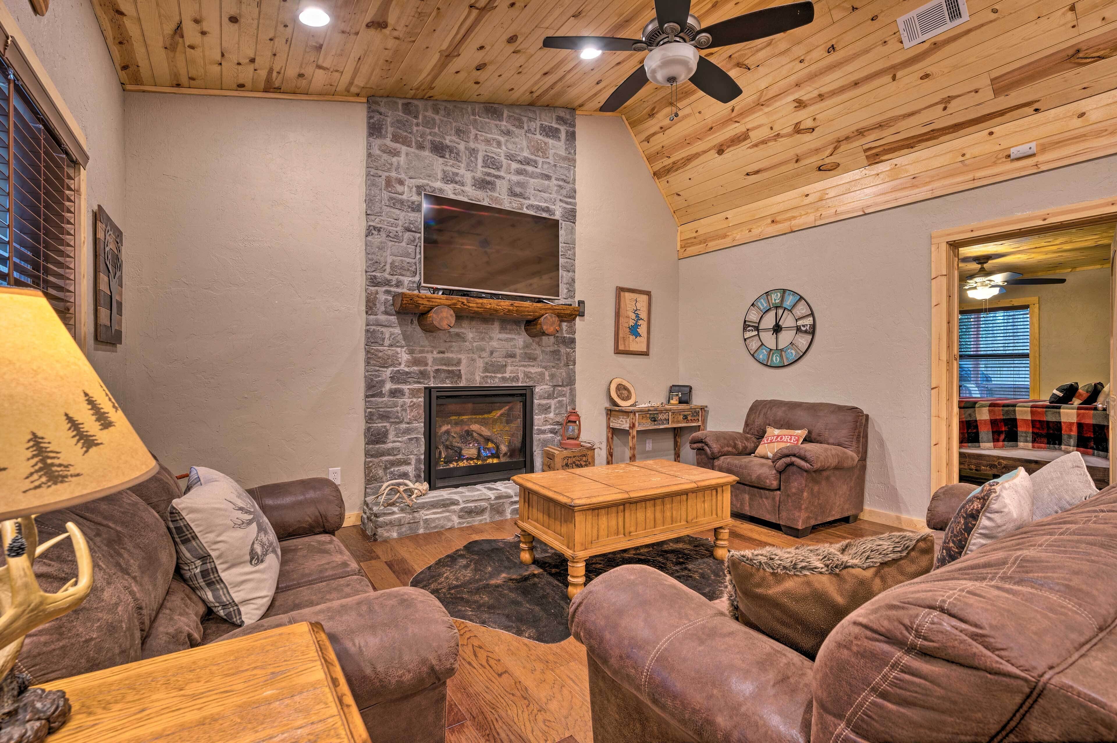 A cozy living room with a stone fireplace, leather sofas, a wooden coffee table, and a ceiling fan.
